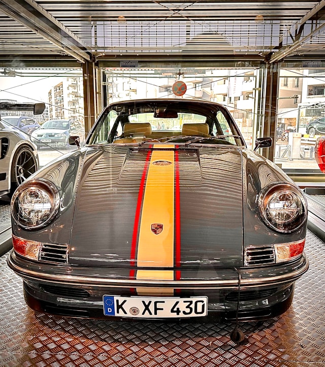 Front view of a gray classic Porsche 911 with a yellow and red center stripe